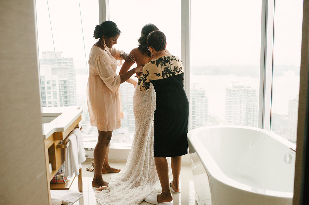 mom and sister helping bride get dressed with skyline